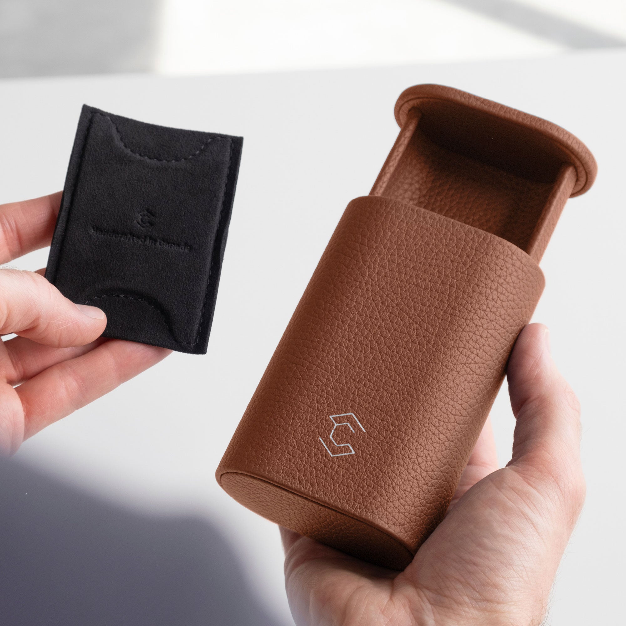Man holding tan leather Oscar Watch roll in one hand and the card insert to hold the watch in place in the other hand.